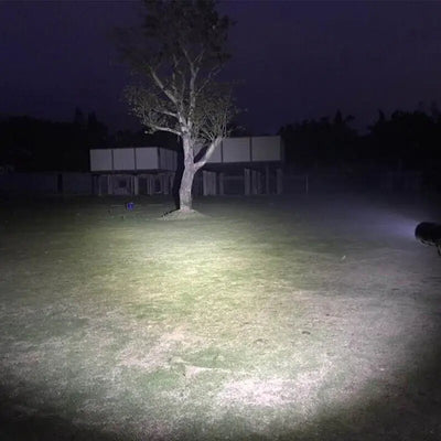 Super Bright 90000LM LED Tactical Flashlight Zoomable illuminating a large outdoor area at night with intense white beam. Ideal for tactical and emergency use.