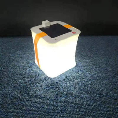 Waterproof Inflatable LED Camping Lantern glowing brightly on a carpeted surface, featuring a solar panel and orange strap for portability.