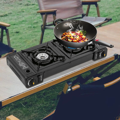 Butane Camping Stove Portable Double Burner Butane Stove with auto ignition, shown cooking stir-fry outdoors on a wooden table with camping chairs nearby.